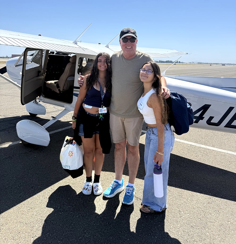 A man standing in between two younger women standing in front of a small plane.