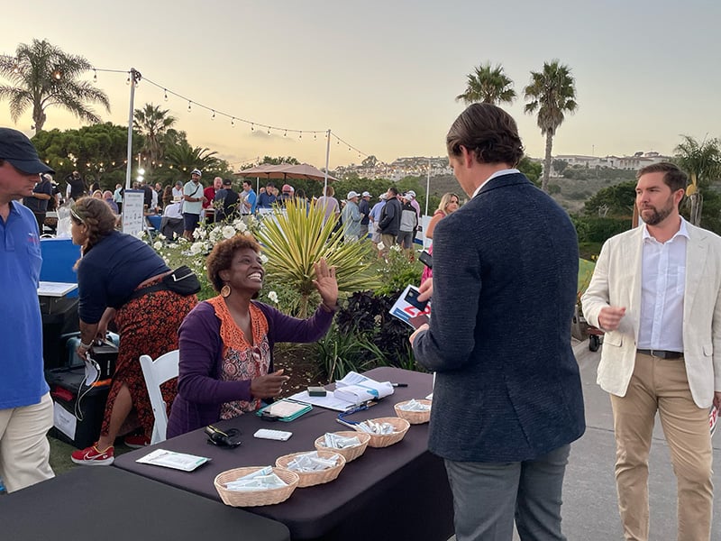 Man standing at a table registering for a golf event with a woman sitting at the table smiling at him.