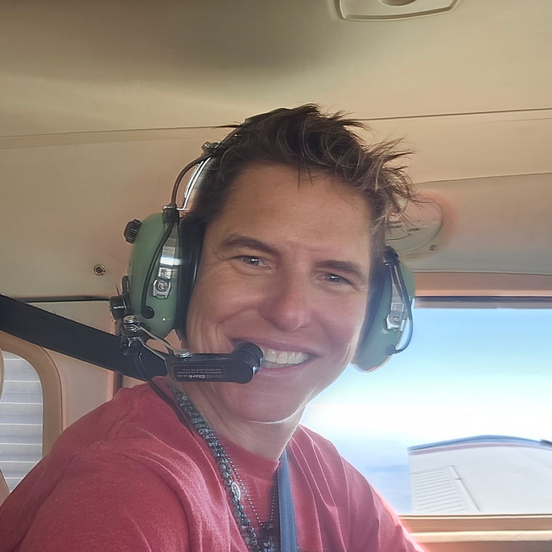 Woman wearing pilot head gear while sitting in an airplane turned smiling at the camera