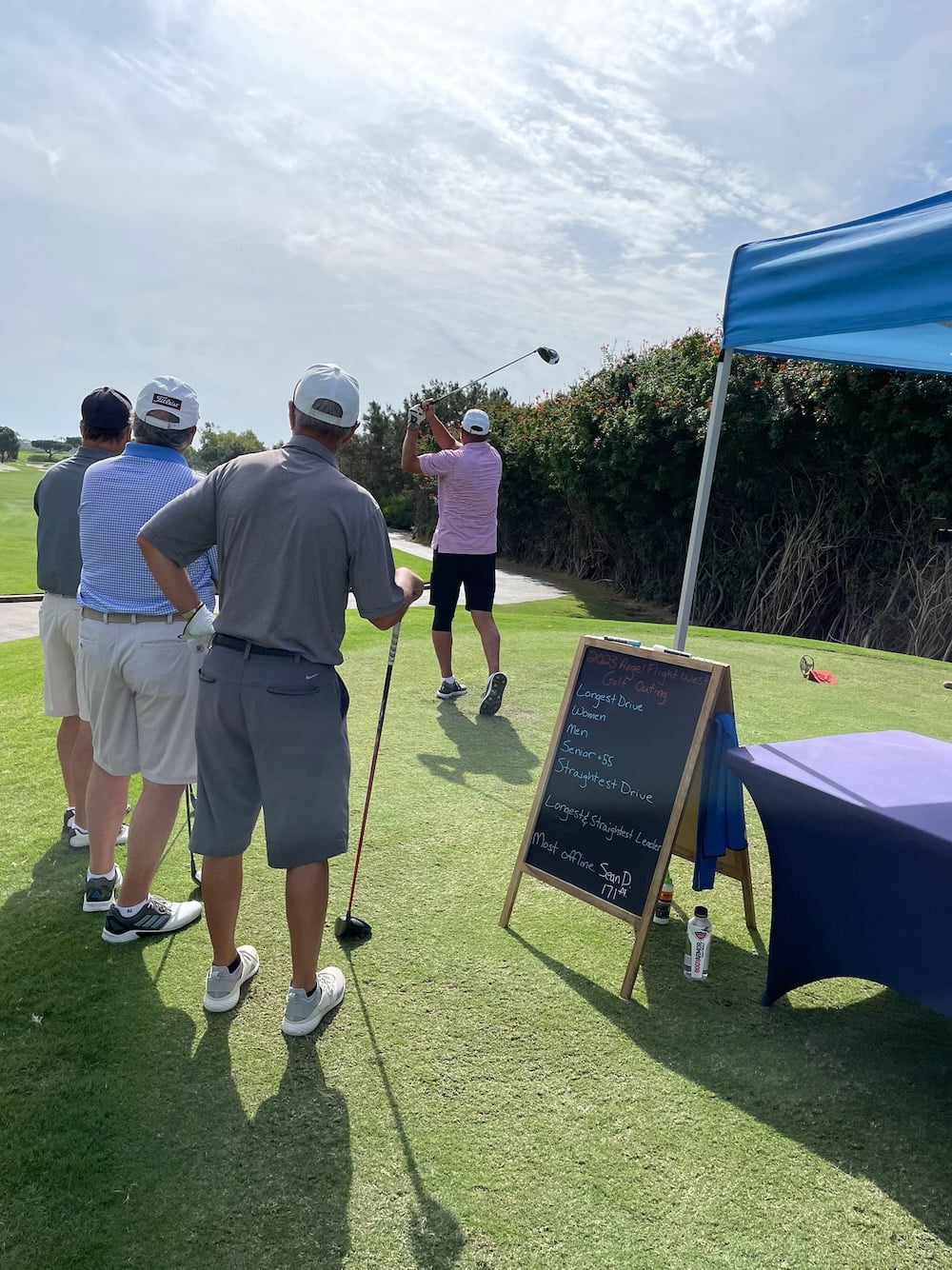 Group of men standing and watching another tee off at a golf course.