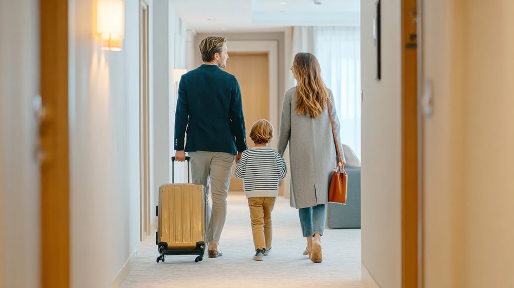 Family walking down a hotel hallway with their suitcases.