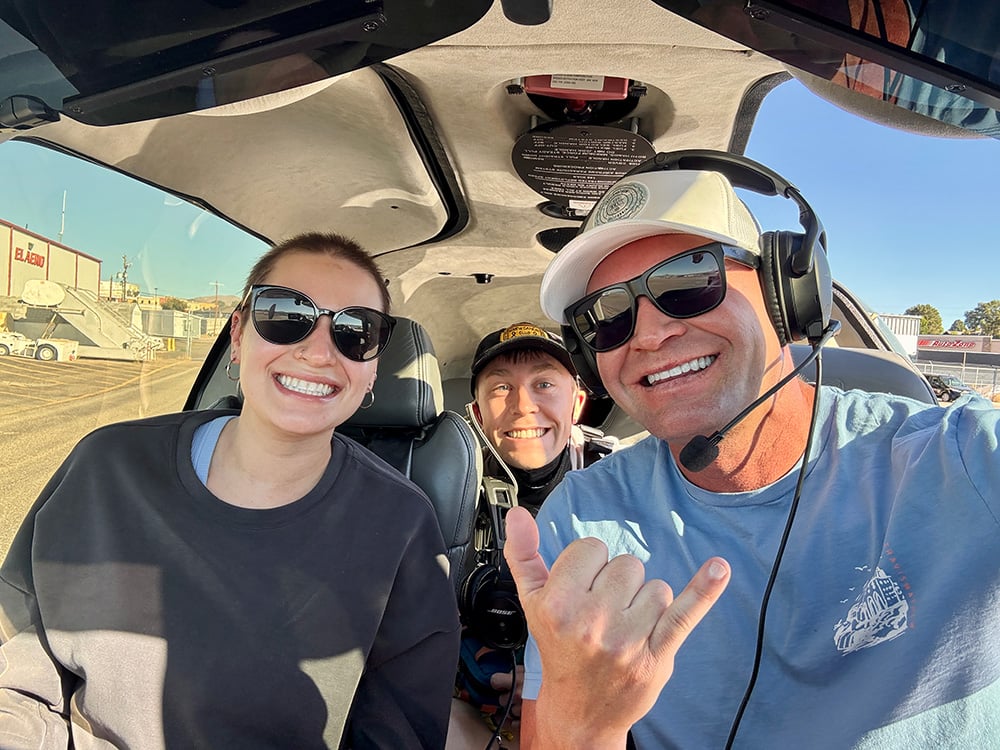 Pilot and two other people sitting in an airplane smiling for the camera.
